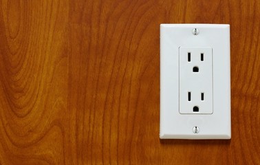 A white power outlet with a double plug connection attached to the side of a shiny wooden counter with attractive wood grain patterns.