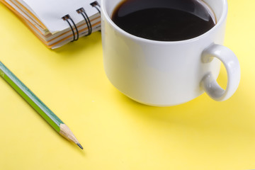 Top view of the freelancer workplace. Modern workplace with a cup of coffee, notebook with pencil, yellow desktop background