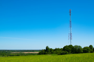 Cell tower on a background of bright blue sky and green grass on a sunny day.