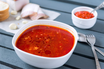  plate of borscht, bacon, soup, ketchup, bread, spoon, fork on a gray wooden background