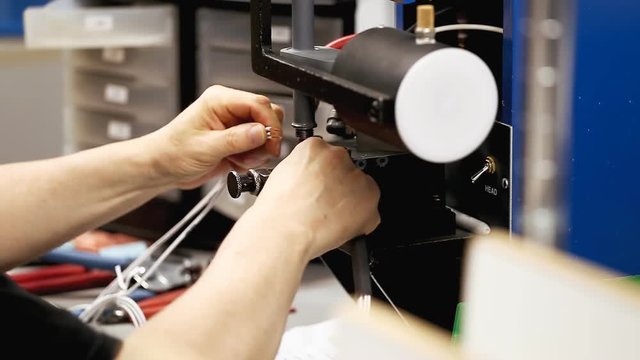 A worker operating an ultrasonic welding machine at a stock-wire factory. Side close-up shot of the hands.