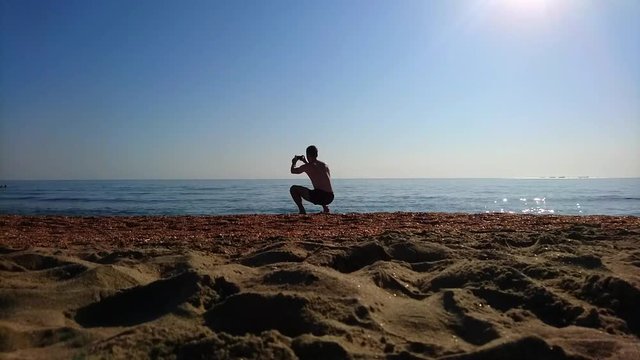Fit Man In Beach Shorts Tacking Making Smartphone Picture Video At Calm Sea Ocean And Clear Blue Sky On Beach Shore In Morning Summer Day