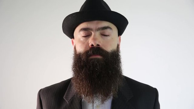A bearded man in a hat wearing traditional Jewish clothing. He smiles looking at the camera.