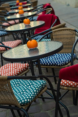 glass tables of an outdoor cafe with pumpkins and colored cushions of chairs