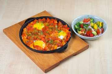 omelet with sweet peppers in a griddle on a wooden board and vegetable salad