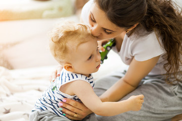 Young mother kissing her baby lying on the bed