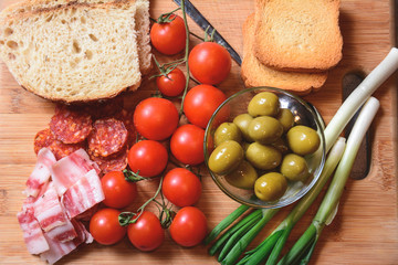 The homemade white bread on a wooden board with organic bacon, cut sausage, cherry tomato, onions and green olives.Toned picture.