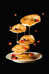 Flying pancakes with honey and currant. Black background.