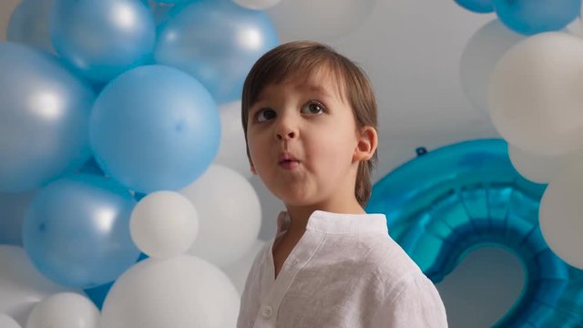 boy of two years in a white shirt sitting at home in blue balloons