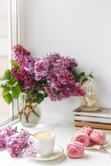 Bouquet of lilacs, cup of coffee, homemade marshmallow and stack of books on window sill Romantic spring morning.