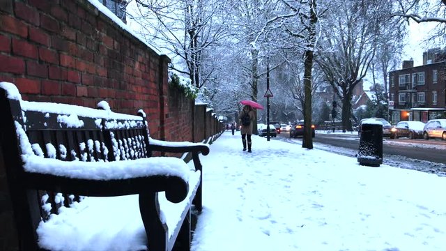 Snowy London city scene with snow piled up on a bench and person with a Red Umbrella