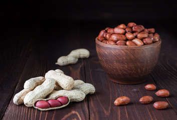 Peanuts in shell on a wooden background and peeled peanuts in a clay bowl, beautiful fresh peanut. Shell peanuts on a table. Shelled and in-shell peanuts.