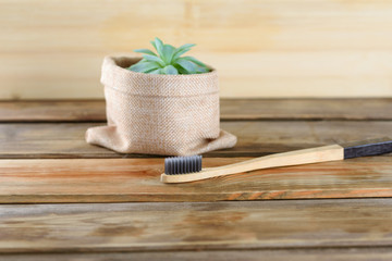 Bamboo toothbrush by the beautiful succulent plant on wooden background.