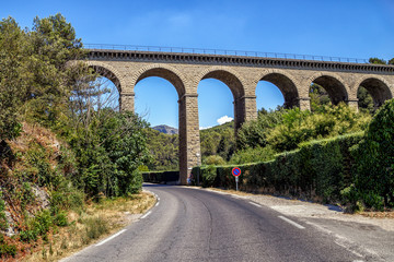 Fototapeta na wymiar Empty road highway and ancient bridge aqueduct at Fontaine de Vaucluse, in a sunny summer day. Provence, France. Copy space. Travel France. 