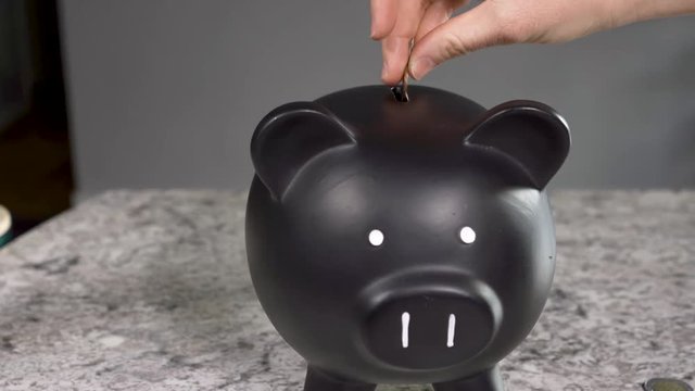 Woman putting coins in black piggy bank