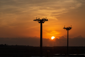 Beautiful sunrise under clouds. Lamp tower of spotlights on the pillars at the airport.