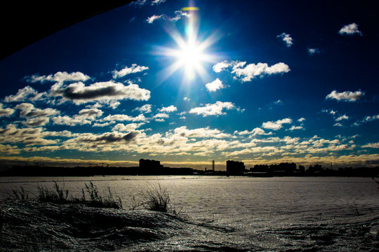 the rays of light, bright sun over the snowy plain with dried grass on the front, the silhouette of a distant city - Powered by Adobe