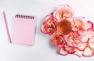 Overhead shot of cup with green tea and colored rose on white background. Lifestyle concept. Mockup with a pink notepad and a pink pencil for drawing. Flat lay. A place for your inscription.