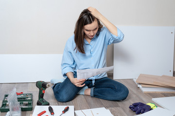 one woman with instructions for assembling furniture sitting on the floor - obrazy, fototapety, plakaty