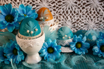 Easter composition with blue Easter eggs, yellow and blue flowers and feathers on a white lace background