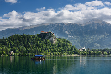 Fototapeta na wymiar Traditional Pletna boat rowing tourists on Lake Bled with Bled castle on cliff and St Martin church Sol massive of Karawanks mountains Slovenia