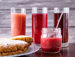 Juice in a glass in the background, a pie on a bowl and jam in a small jar.