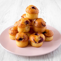 Homemade muffins with cherry on pink plate on a white wooden table, side view. Close-up.