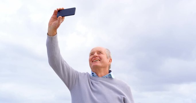 Front view of old caucasian senior man taking selfie with mobile phone at beach 4k
