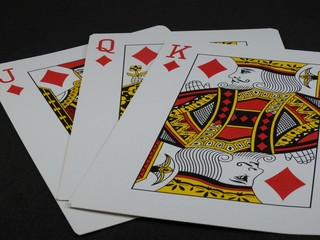 Close-up of three playing cards: King, Queen and Jack of Diamonds on a black background.