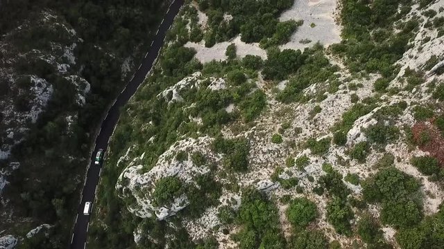 Two Cars driving on a mountain pass. Filmed from top bird's eye view with a drone following them smoothly. Like in GTA game. Summer atmosphere in green forrest und grey rocky french alps landscape