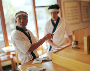 Two Japanese chefs preparing for diners in a traditional restaurant.