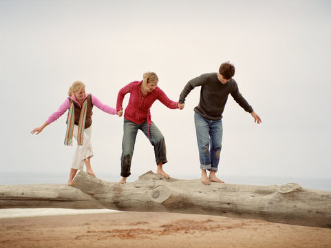 Mid-adult couple with their teenage daughter walking along driftwood on a beach.