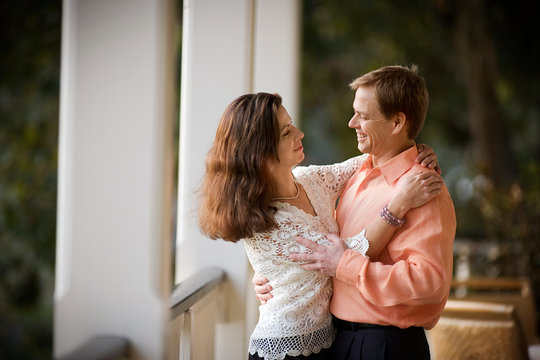 Smiling mid-adult couple dancing together on a balcony.
