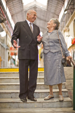 Senior business man standing on steps smiling at his wife while she is holding his arm.