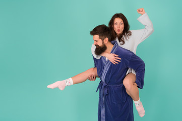 Handsome young man giving his girlfriend piggyback ride. Couple in bathrobes having fun turquoise...