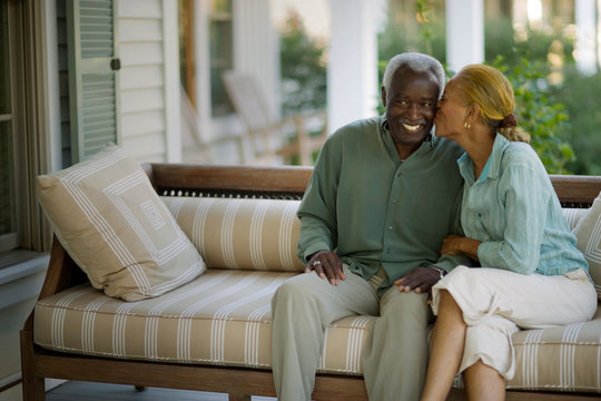 Smiling senior man being kissed by his wife on a porch.