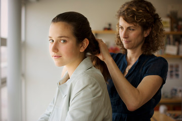 Portrait of a teenage girl getting her hair fixed by her mother inside their home.