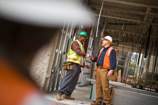 Mature male construction worker shaking hands with a mid-adult co-worker on a building site.