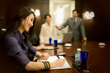 Young adult business woman taking notes for a meeting in a boardroom.