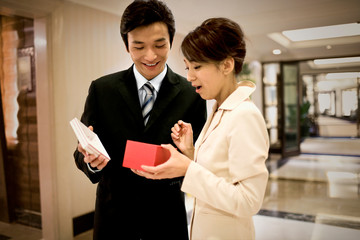 Young adult businessman giving a gift to his girlfriend in a lobby.
