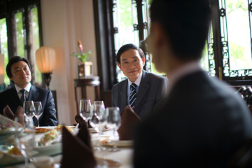 Two businessmen sitting around a dining table with colleagues.