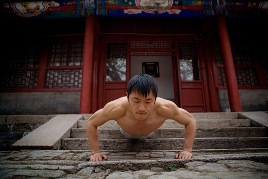 Young adult man doing press ups outside a building.