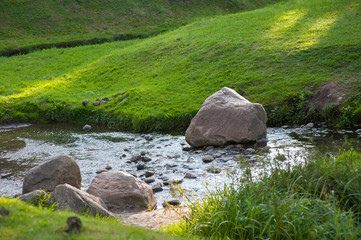 Stones in the river interfere with the flow of water, the lawn by the river
