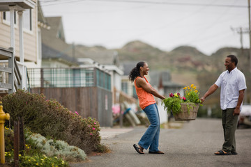 Happy mid-adult couple holding a wooden basket of plants in a suburban street.