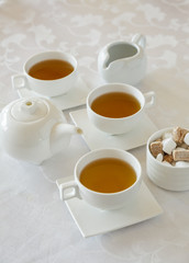 Obraz na płótnie Canvas Afternoon tea service with hot tea cups, sugar cubes, and tea pot on white linen table cloth