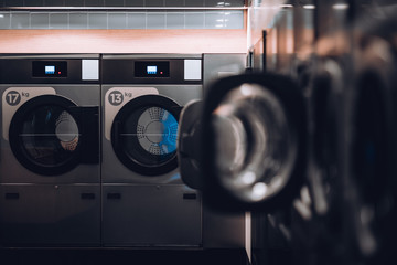 A dark modern room of a publiс laundry with perpendicular rows of washing machines with some of...