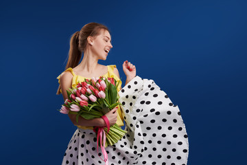 Perfect gift. Wonderful flowers on Womens Day. Tender smiling brunet woman poses with colorful tulips, looks happily, isolated over blue studio background. Space for text