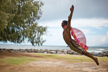 Man leaping with a beach towel for a cape.