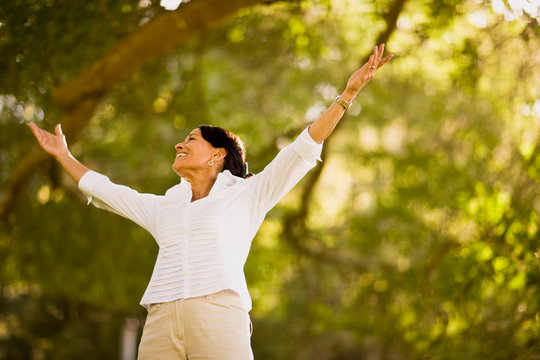 Mature woman standing in a park with her arms outstretched