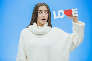Young pretty girl dressed in white clothes. During this time it stands on a blue background. Holds a word of love in hands.